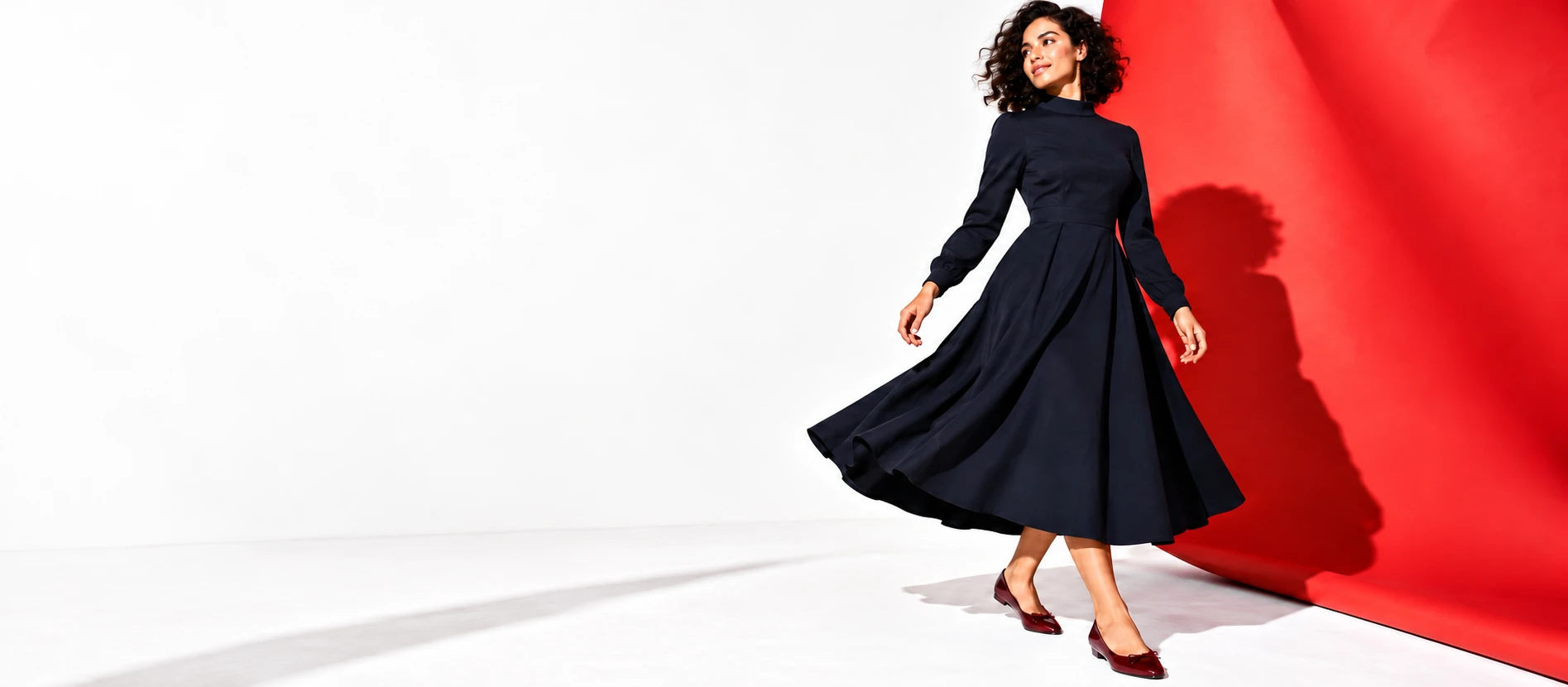 A woman in a long-sleeved navy midi dress against a coral studio backdrop